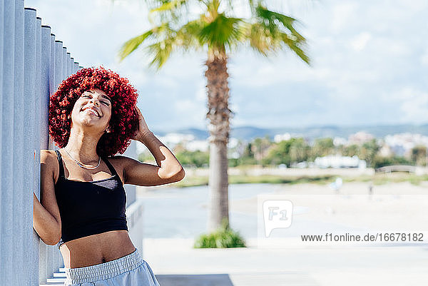 Frau mit rotem Afro-Haar stehend mit Strand im Hintergrund.