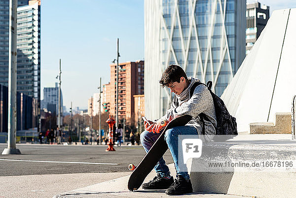 Junger Backpacker-Teenager sitzt im Freien und benutzt ein Smartphone