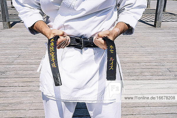 Karate-Mann beim Binden des Knotens seines schwarzen Gürtels