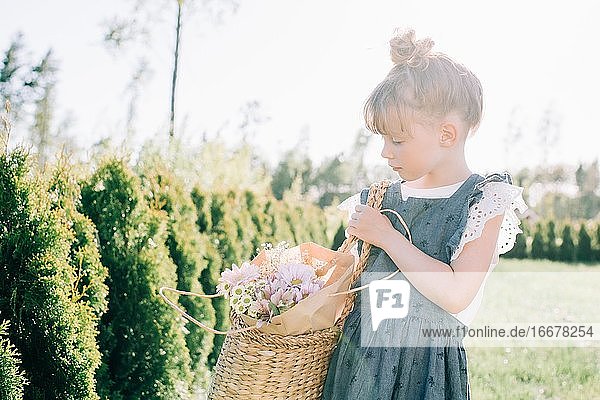 junges Mädchen trägt im Sommer schöne Blumen in einem Korb nach draußen