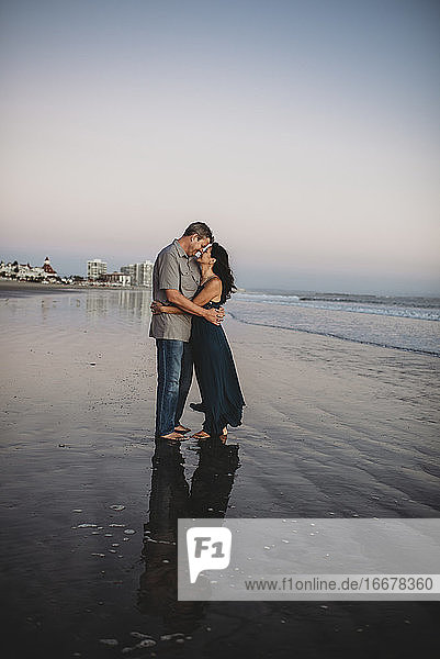 Barfuß liebendes Paar Mitte 40 am Strand  das sich von Angesicht zu Angesicht umarmt