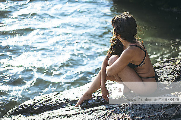 Junge Latina Frau sitzt am Meer zur goldenen Stunde im Sommer