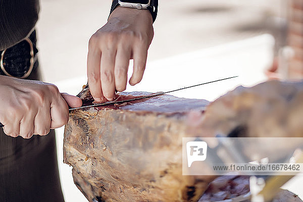 Frau schneidet iberischen Schweineschinken mit einem Schinkenhalter und einem Messer