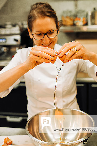 Weiblicher Koch beim Eierschlagen in einer Restaurantküche  Lifestyle-Clo