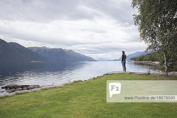 Ein Mann trinkt eine Tasse Kaffee und blickt auf einen Fjord in Norwegen
