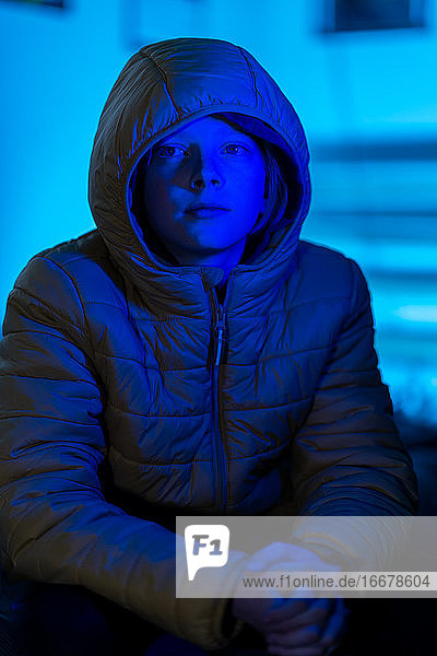 Porträt eines jungen Menschen  der in einem nur mit blauem Licht beleuchteten Raum sitzt