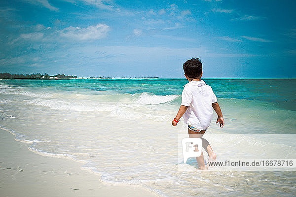 Little boy walking at the beach watching Caribbean ocean