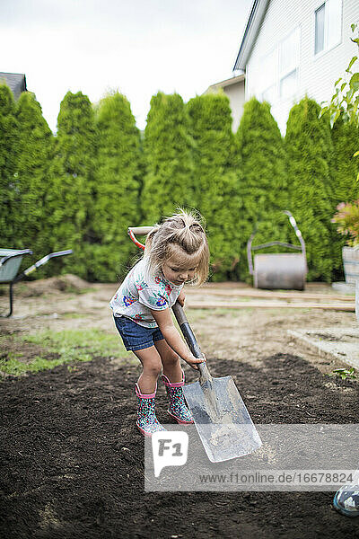 Zweijähriges Mädchen beim Schaufeln von Erde in ihrem Garten.