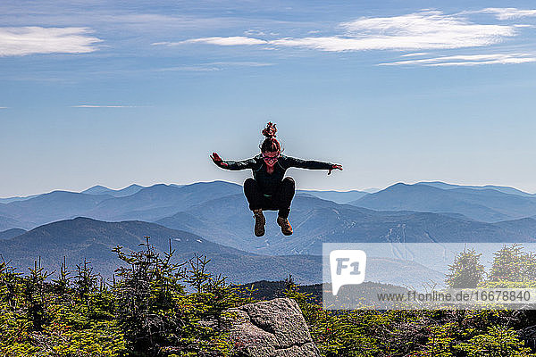 Junge sportliche Frau  die auf einen Berggipfel springt.