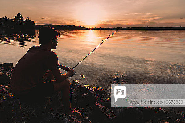 Adolescent boy fishing on shore of lake at sunset in Ontario  Canada.