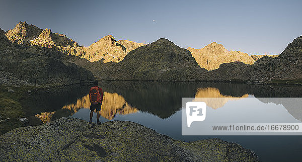 Ein junger Mann mit Rucksack betrachtet die Spiegelung im See  Sierra de Gredos