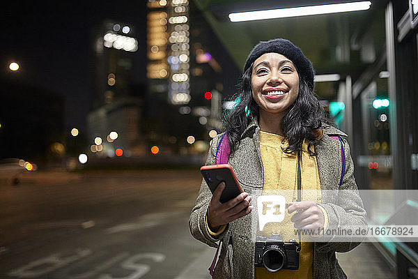 lächelnde Frau  die nachts auf der Straße steht und sein Handy benutzt