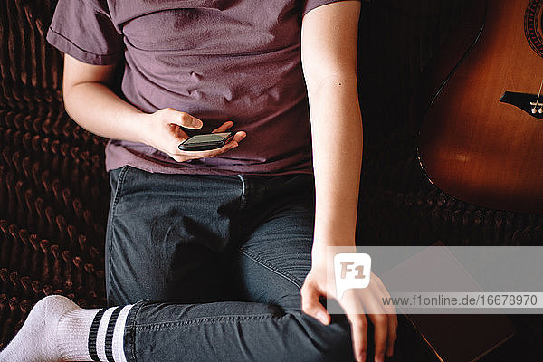 Jugendlicher benutzt sein Smartphone  während er zu Hause auf dem Sofa sitzt