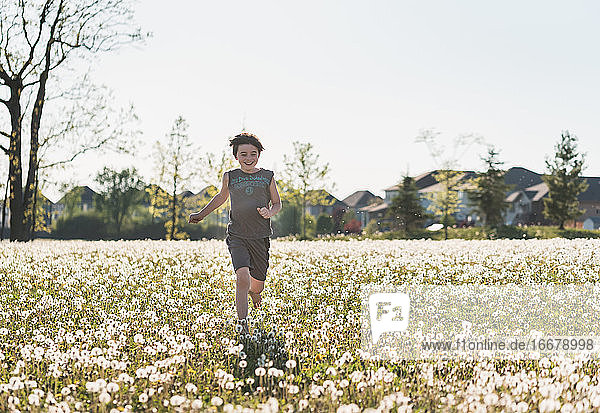 Boy running in a grassy field full of dandelions on summer day.