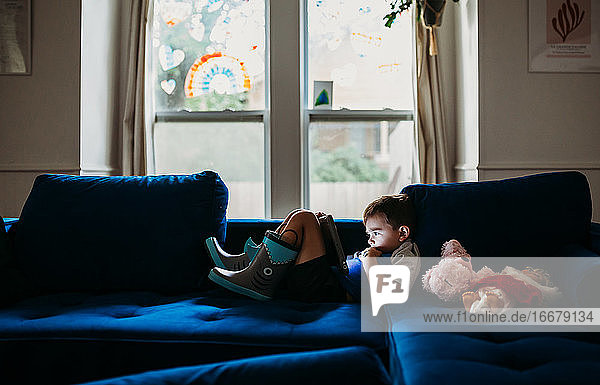 Junge im Vorschulalter liegt auf der Couch und schaut Tablet an einem regnerischen Tag