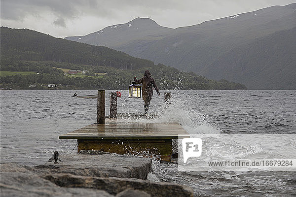 Eine Person mit einer Laterne an der Kante eines Docks in Norwegen