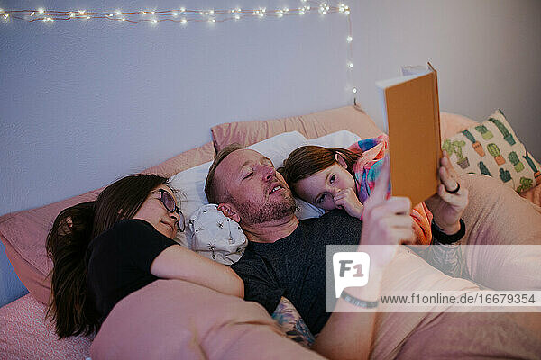 Vater liest und kuschelt mit den Kindern im Bett