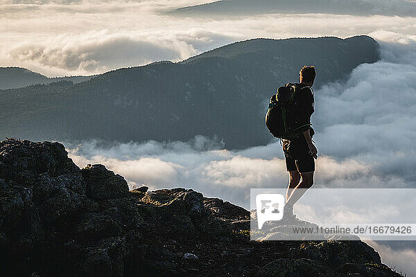 Männlicher Wanderer auf dem Gipfel blickt auf den Berg  der sich über den Wolken erhebt  Maine