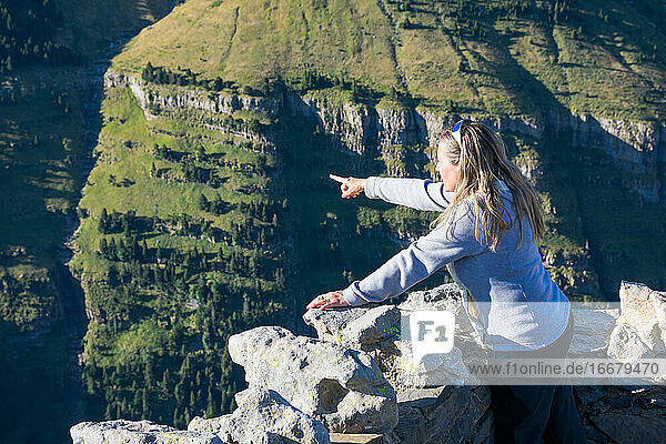 one woman pointing with her finger at a place of Ordesa national park. She is admiring from the top of a balcony mountain the whole valley  the green forests  the rocks and the hills Horizont