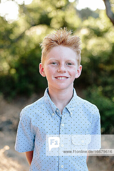 Ein süßer rothaariger Junge mit Sommersprossen lächelt für ein Porträt im Freien