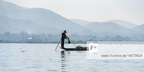 Fisherman using fishing net on boat against mountains  Lake Inle  Nyaungshwe  Myanmar