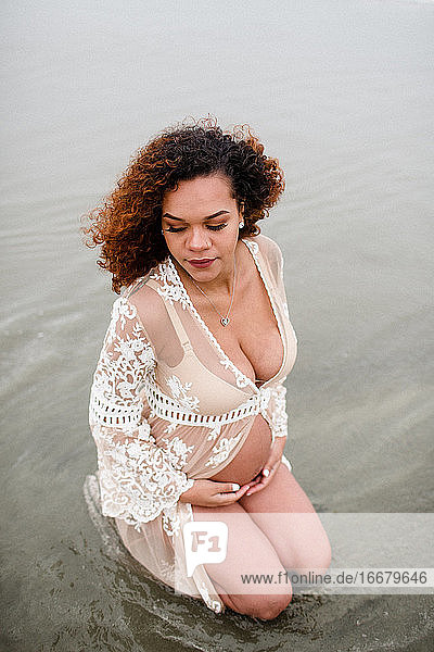 Junge schwangere Frau kniend im Wasser am Strand