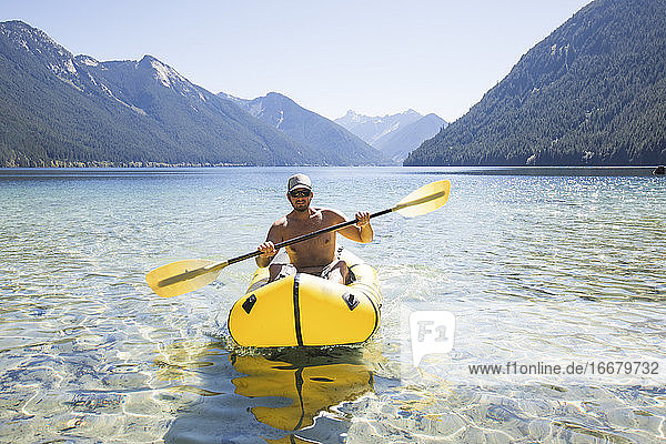 Shirtless man paddling inflatable packraft or kayak.