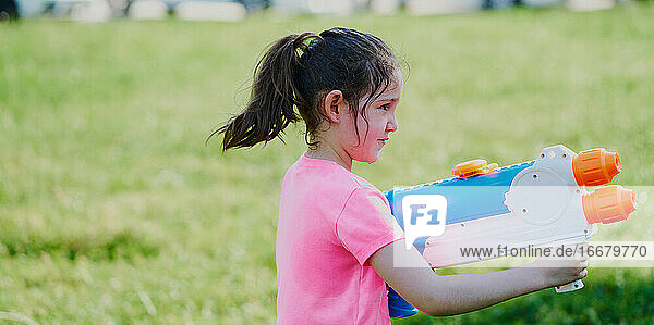 Mädchen spielt mit einer Wasserpistole im Garten und trägt ein rosa T-Shirt