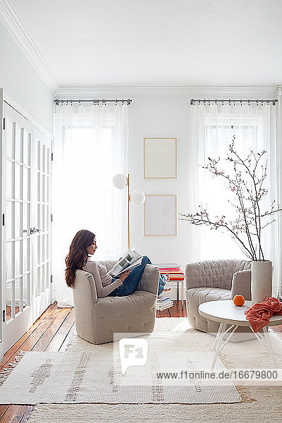 Frau  die in einem modernen Stuhl in einem hellen  weißen Wohnbereich liest