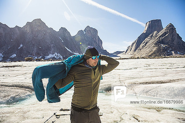 Mountaineer puts on warm jacket in glacial mountain landscape.
