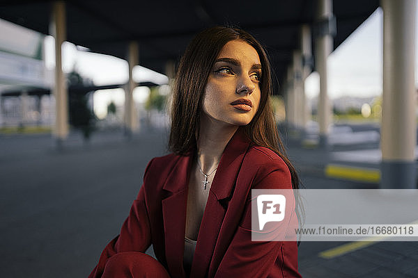 Frau im roten Anzug sitzt am Busbahnhof