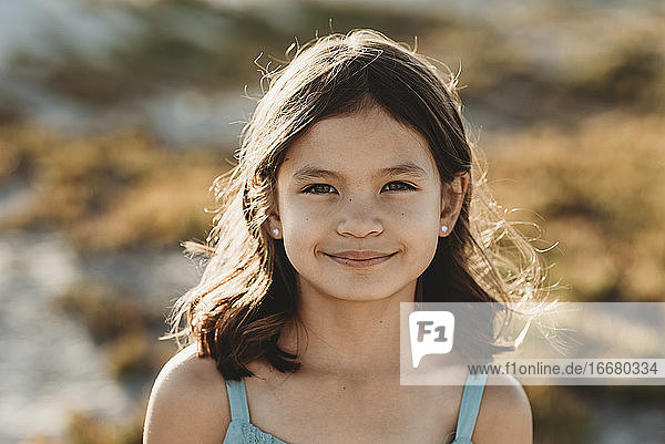 Lächelndes 8-jähriges Mädchen mit Sonnenlicht  das durch ihr dunkles Haar spielt