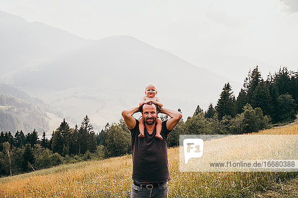 Man with baby on shoulders smiling with views of the mountains