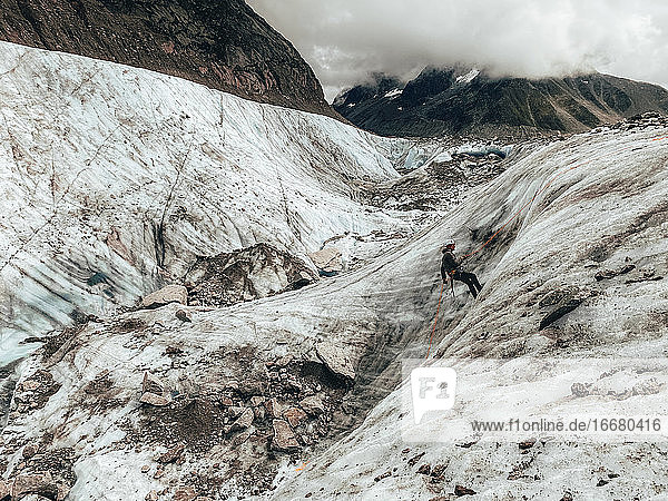 Landschaftsaufnahme eines Bergsteigers beim Abseilen auf einem Gletscher bei bewölktem Himmel