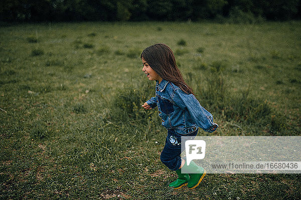 Lachendes Mädchen  das in Regenstiefeln durch ein Feld läuft
