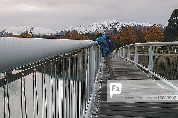 Frau blickt von einer Brücke auf den Lake Tekapo mit Bergen im Hintergrund