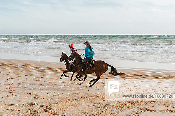 Zwei Frauen reiten auf andalusischen Pferden am Strand in Spanien