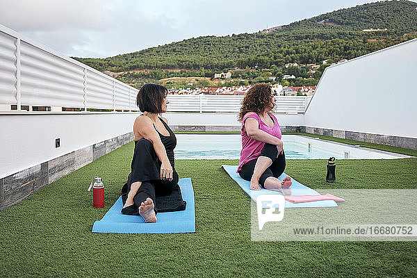 Zwei Frauen üben Yoga auf der Terrasse des Hauses  Marichi-Haltung