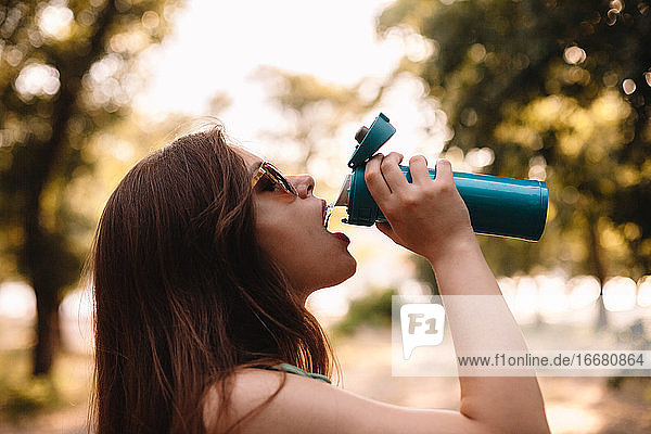 Junge Frau trinkt im Sommer im Park Wasser aus einer wiederverwendbaren Flasche