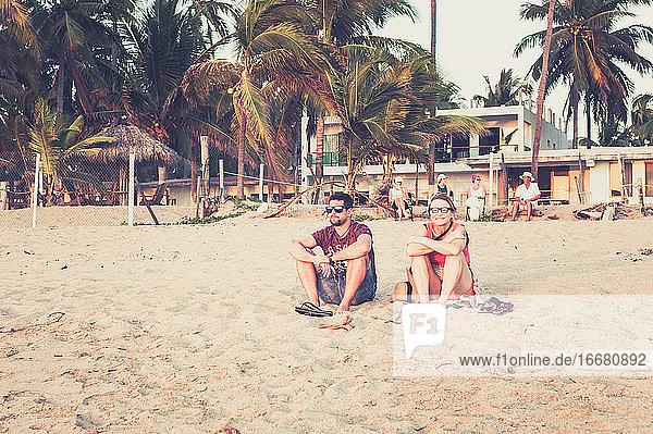 Mother and Son sitting in sand in Mexico at sunset with palm trees
