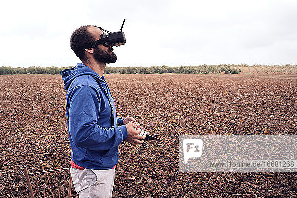 junger Mann mit schwarzem Bart fliegt Drohne und beobachtet ihn durch eine Brille
