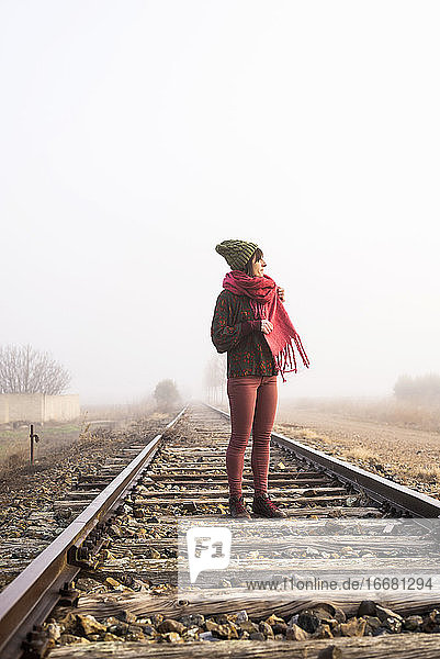 Nachdenkliche Frau  die auf einer nebligen Bahnstrecke steht und wegschaut