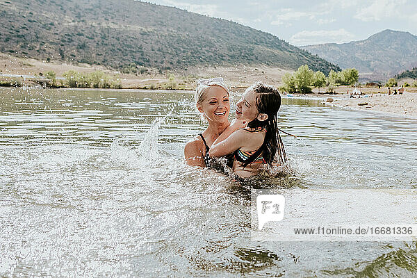 Portrait of happy mom and daughter playing in a lake on a sunny day