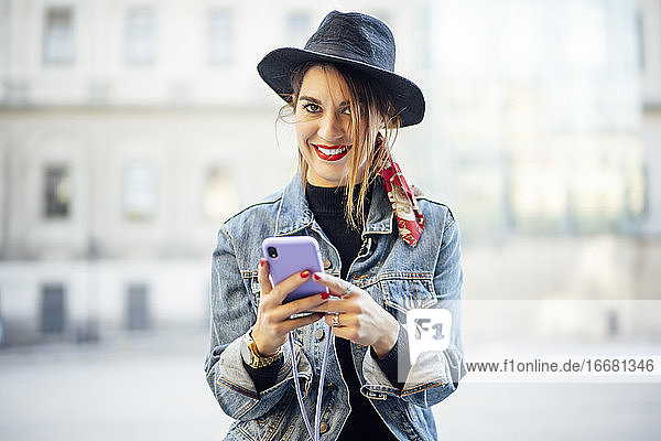 Schöne Frau im Herbstkleid mit Hut  die ein Mobiltelefon benutzt
