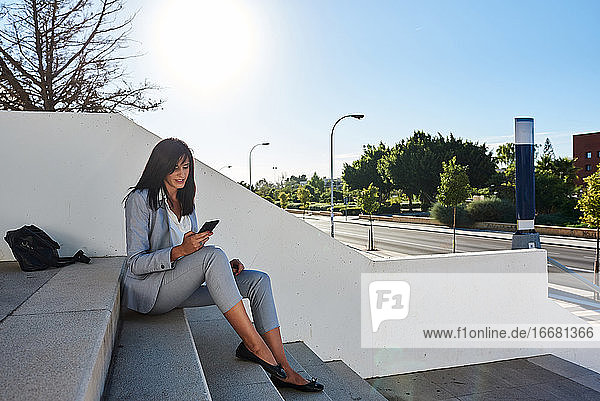 Geschäftsfrau auf einer Treppe sitzend mit Smartphone in der Hand.