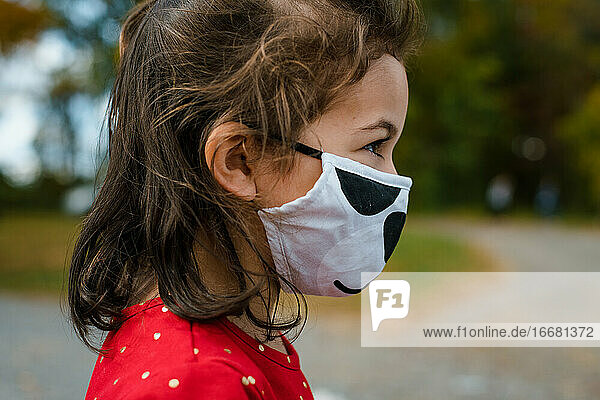 Mädchen im Vorschulalter trägt im Herbst draußen einen Gesichtsschutz