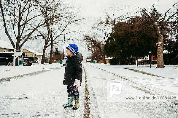Young boy standing in snowy road wearing jacket in winter