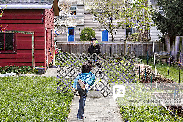 Ein Junge und sein Vater spielen behelfsmäßig Tennis im Hof über einem Holzzaun
