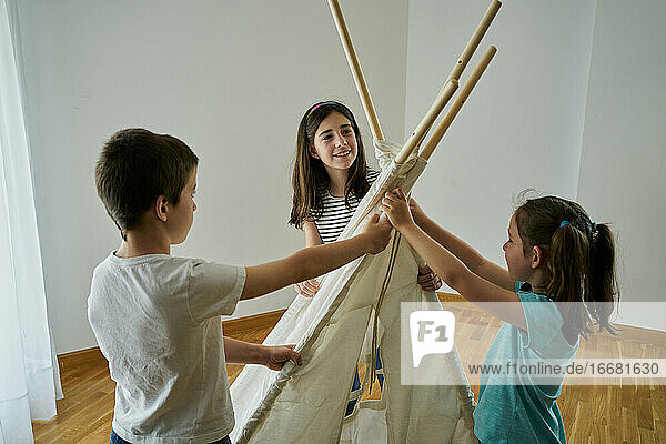 Kinder legen die Stöcke  um ein Tipi-Zelt in ihrem Haus zu bauen. Kreativitätskonzept