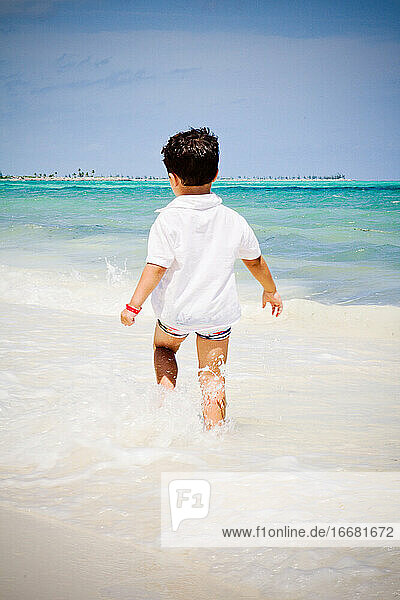 Little boy walking on the beach watching the Caribbean ocean